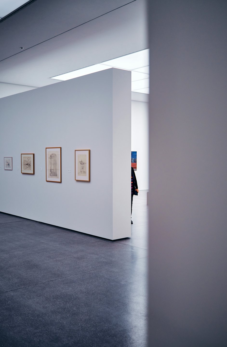 Person walks past framed drawings in a modern art gallery.